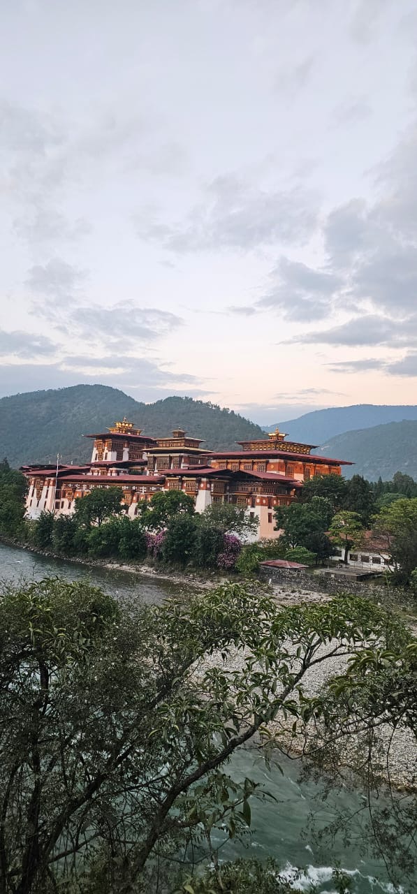 A Bhutanese dzong beside a river nestled among green hills at dusk