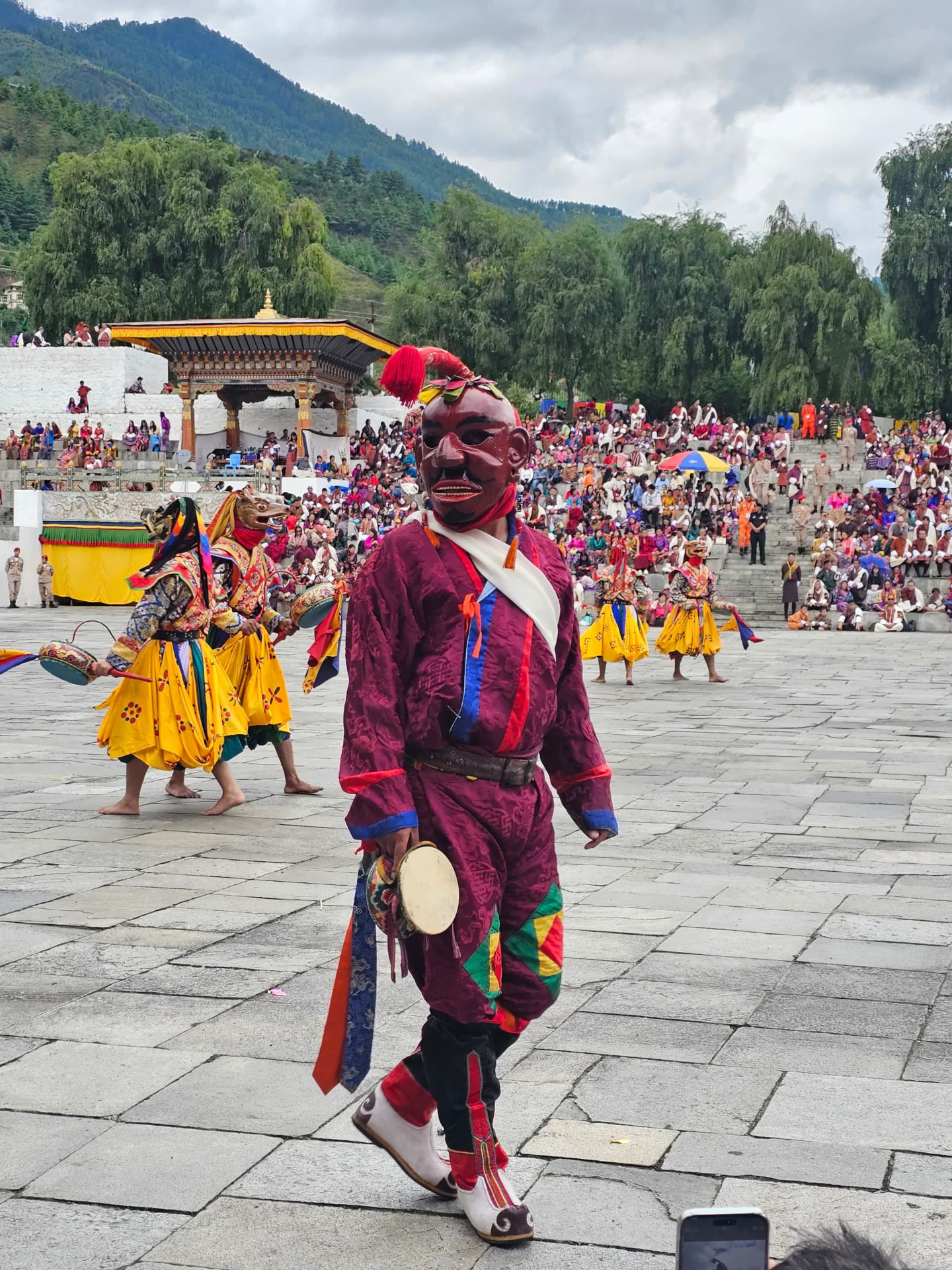 A masked festival dancer in colourful brocade performing before a crowded festival courtyard
