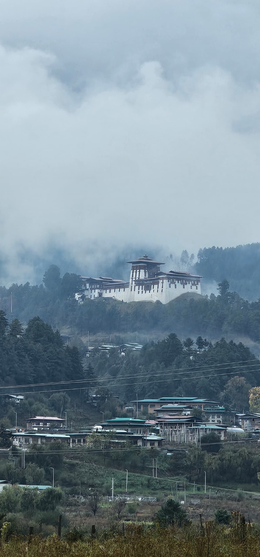 A distant white dzong rising above a misty forested valley
