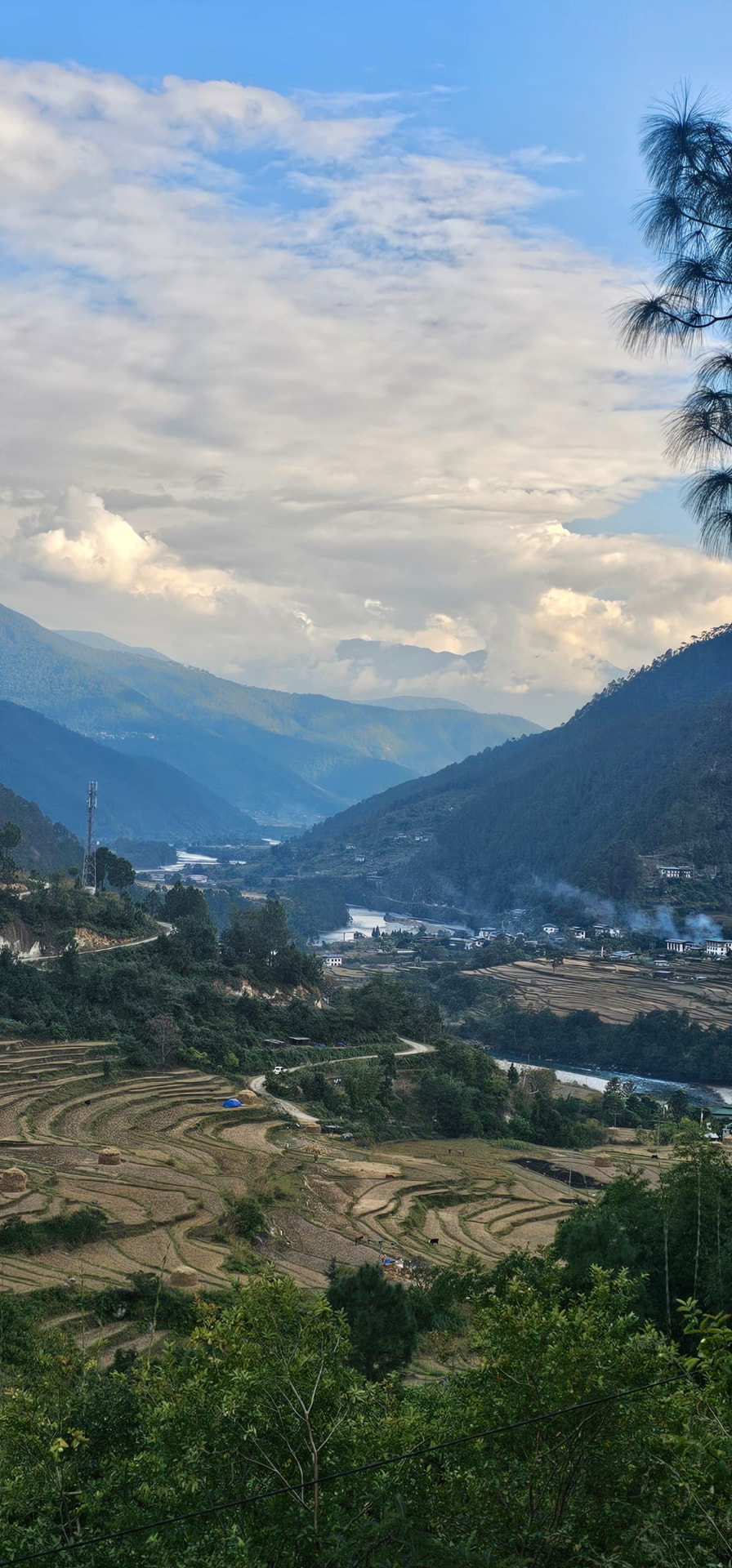 Terraced fields and a winding river beneath layered mountain slopes and a cloud-filled sky