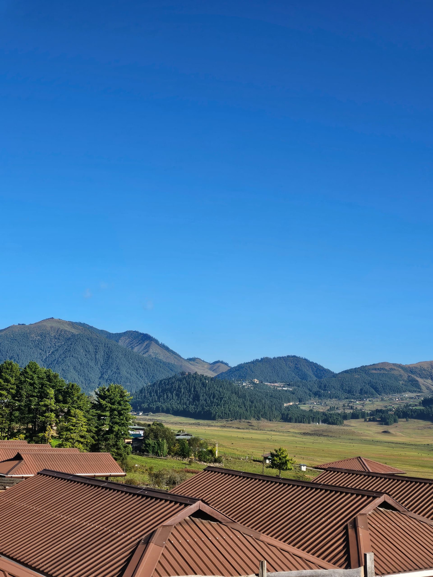 A Bhutanese mountain valley with rooftops under a clear blue sky