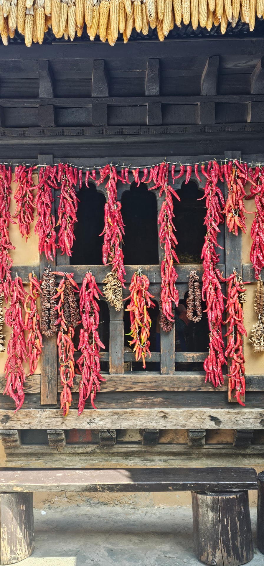 Red chillies and golden corn drying across the timber windows of a traditional Bhutanese home