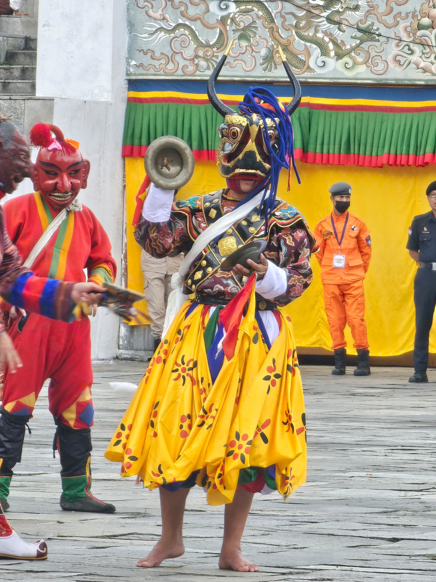 Colourful masked tshechu dancers performing in front of a festival backdrop