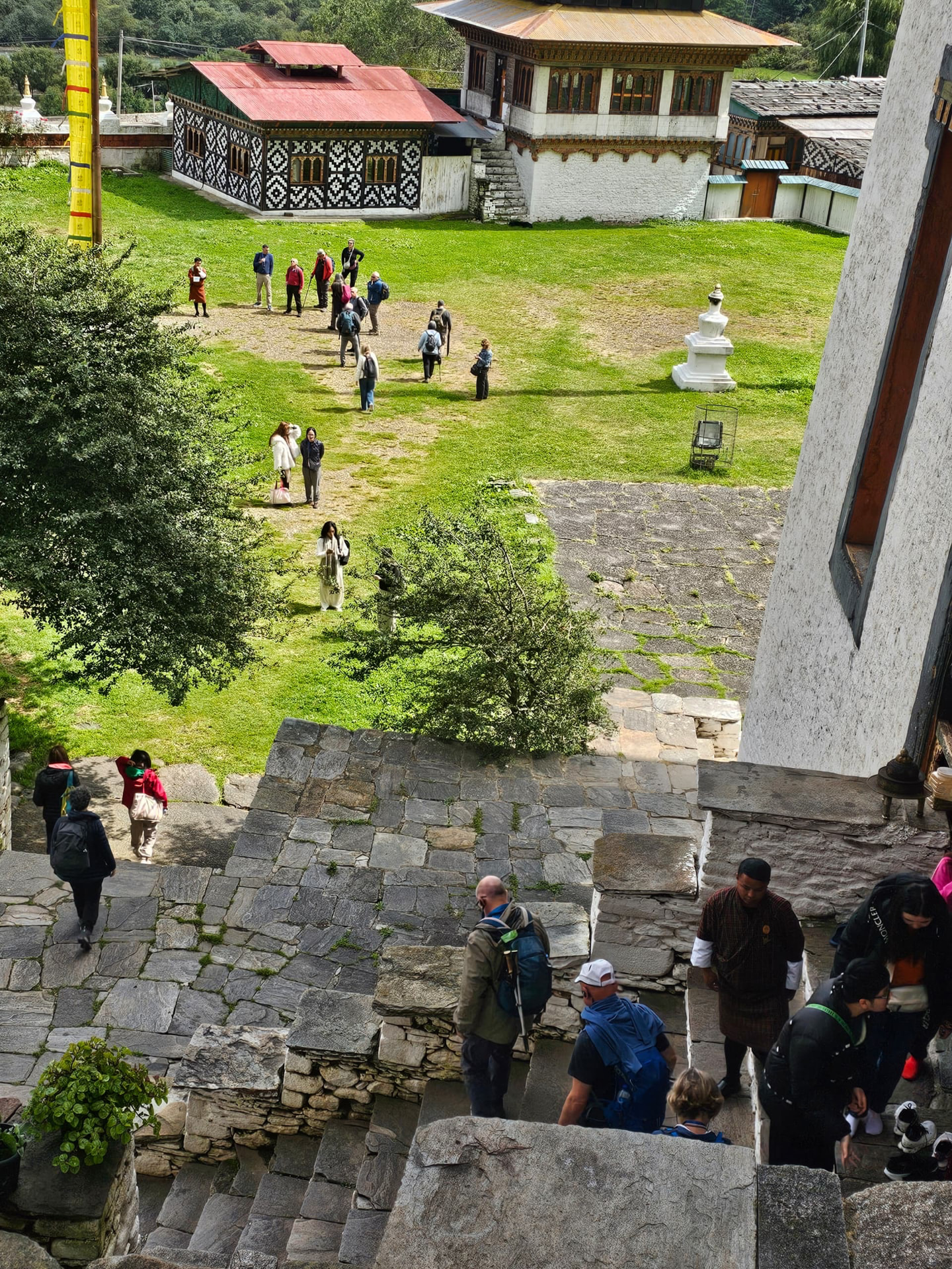 Visitors walking through a green temple courtyard and up stone steps among traditional Bhutanese buildings