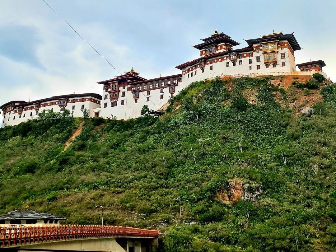 Wangdue Phodrang Dzong rising above a forested ridge, seen from the cantilever bridge below